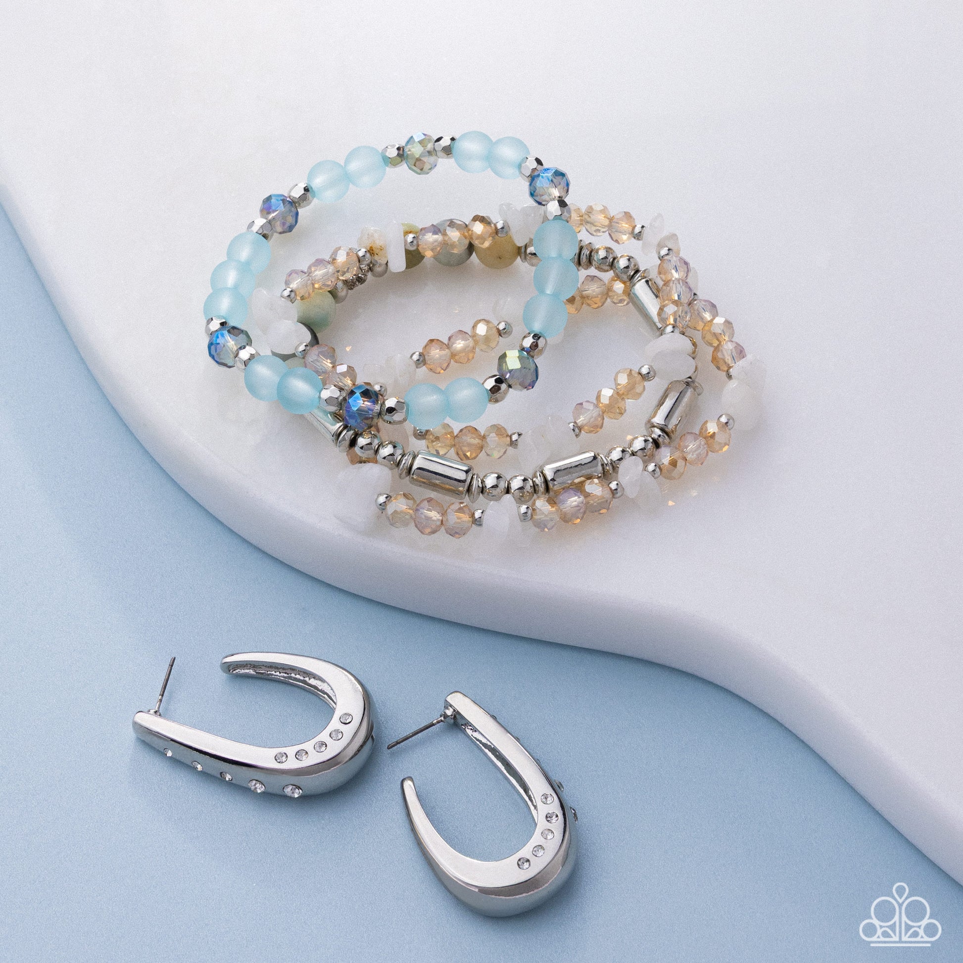 Beaded bracelet and silver hoop earrings on a light blue background