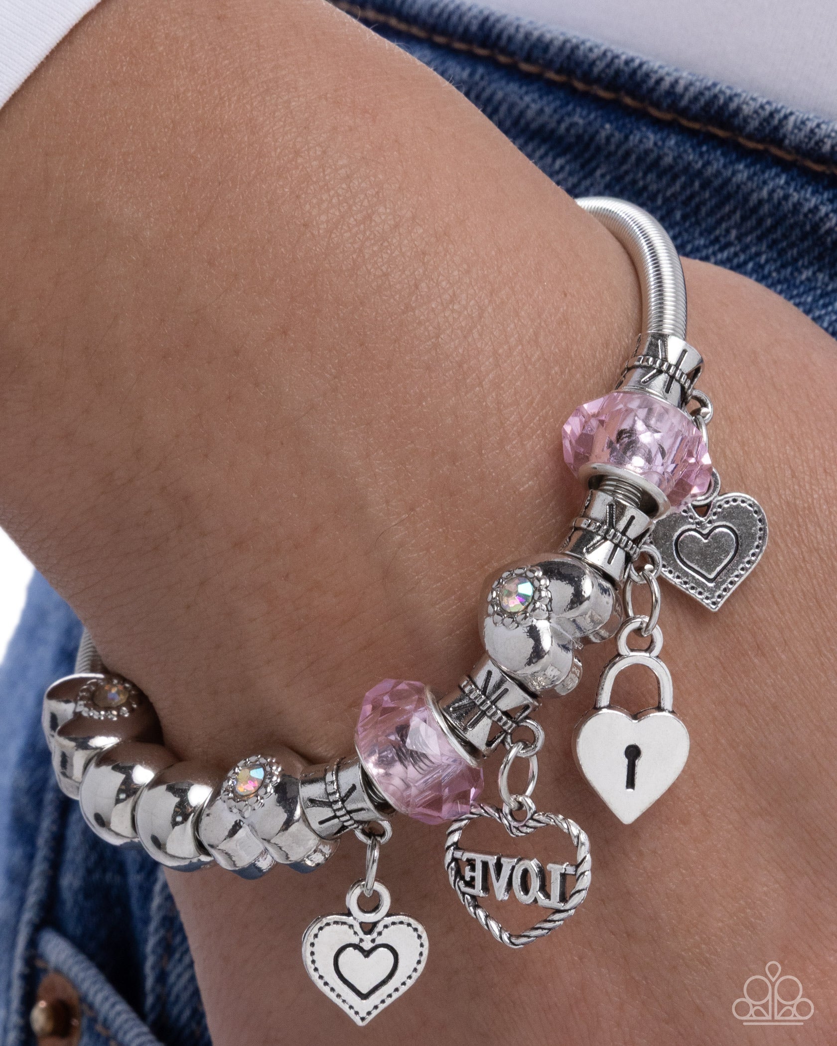 Silver bracelet with heart and lock charms on a wrist against denim fabric