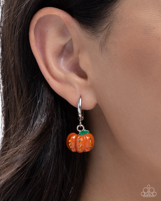 Orange pumpkin-shaped earring worn on an ear with a neutral background