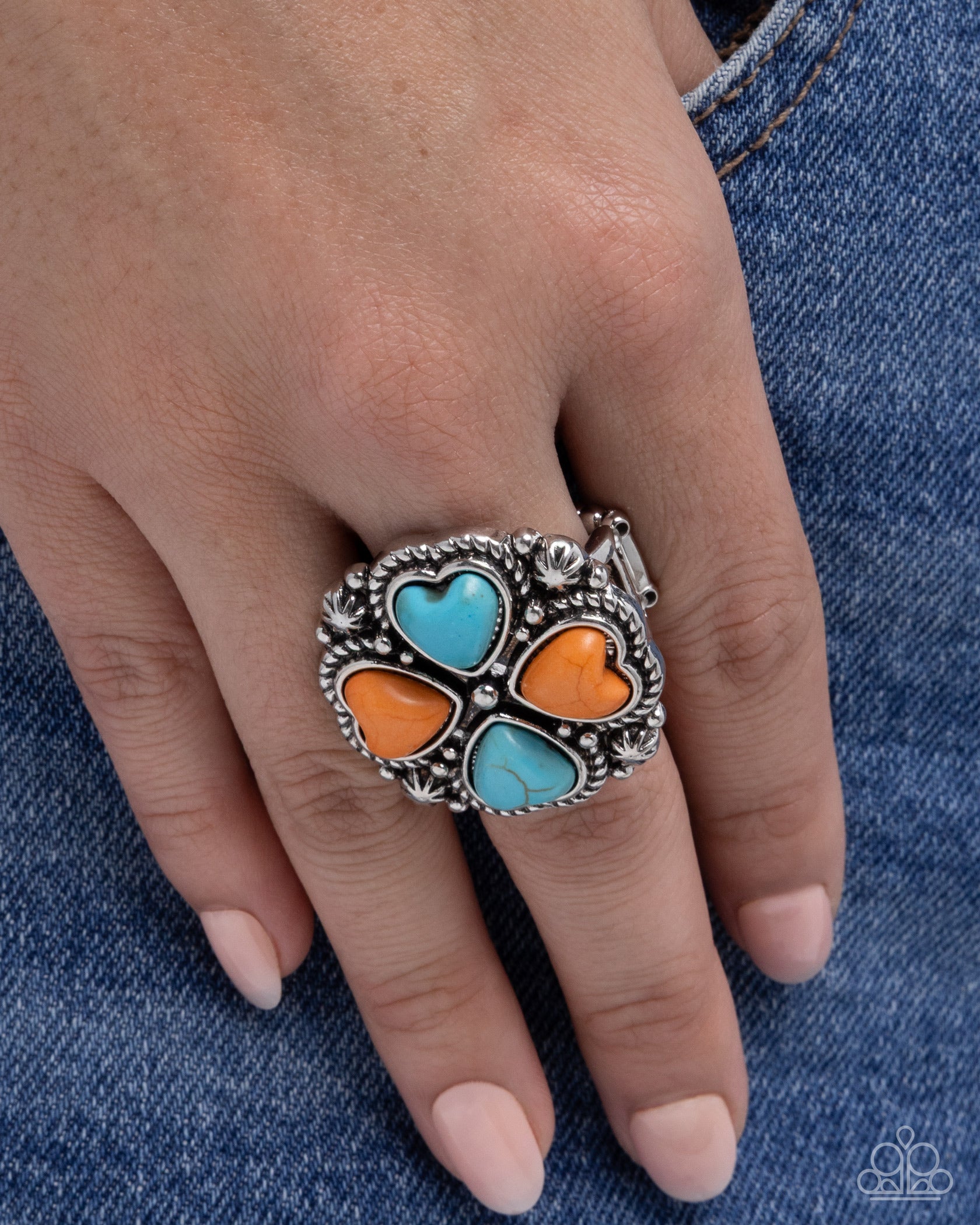 Silver ring with colorful heart stones on a hand against a denim background