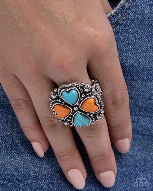 Silver ring with colorful heart stones on a hand against a denim background
