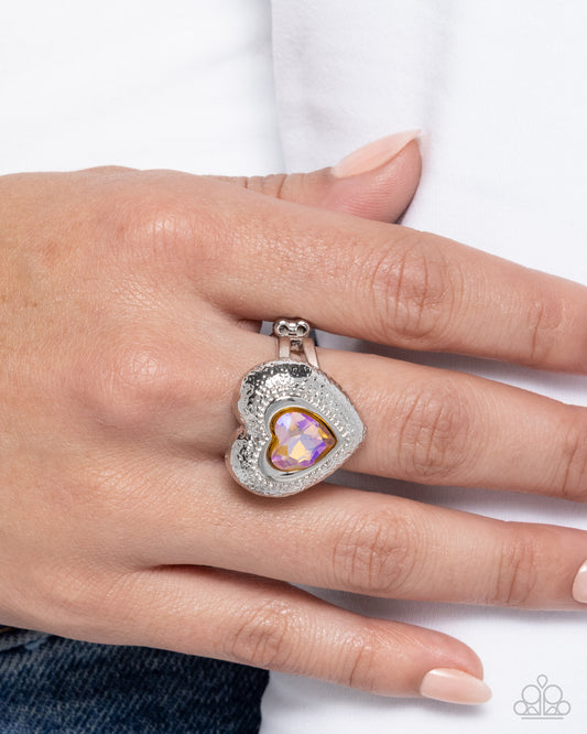 Heart-shaped ring with a colorful gemstone on a hand against a white background