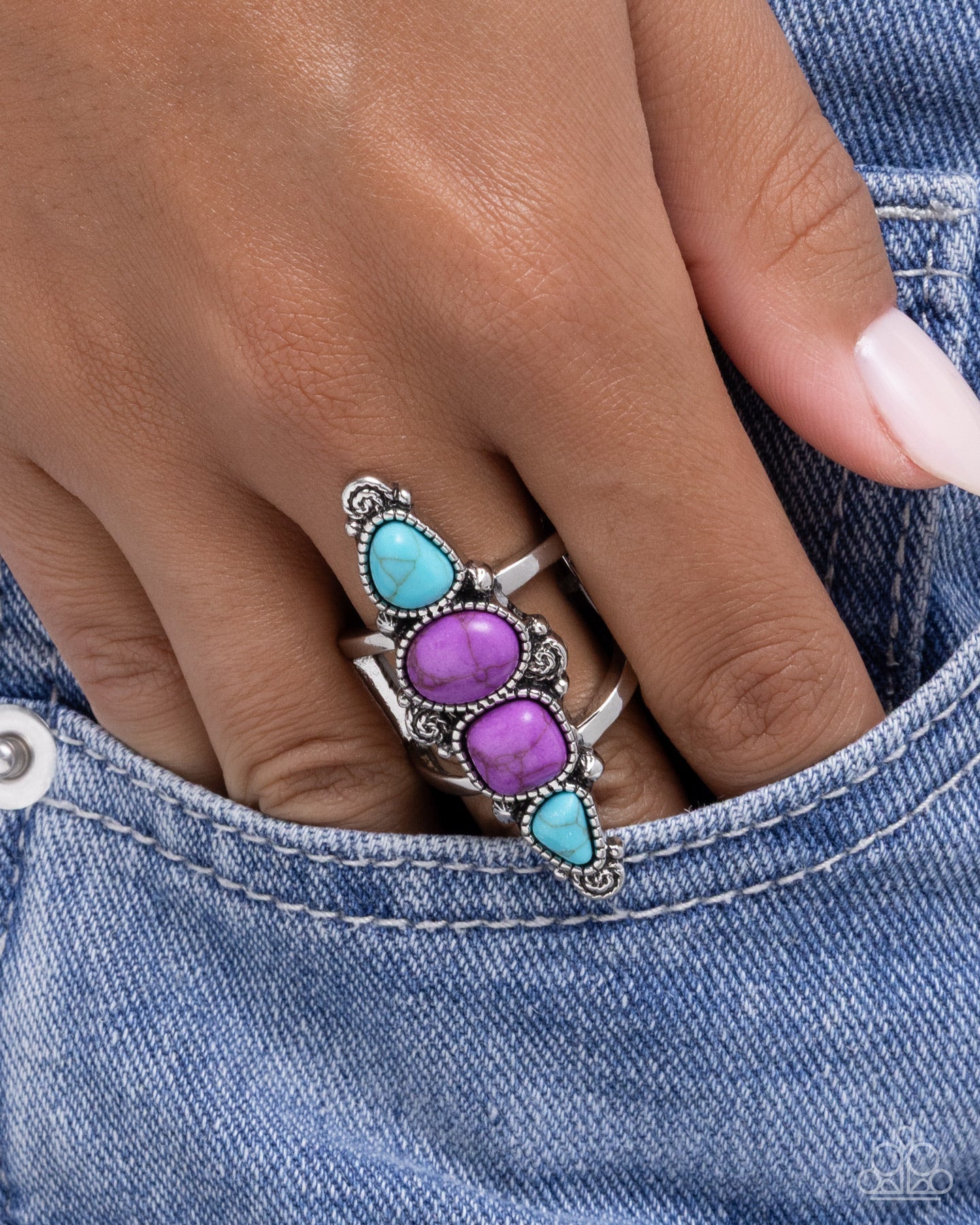 Silver ring with purple and turquoise stones on a hand wearing denim jeans.