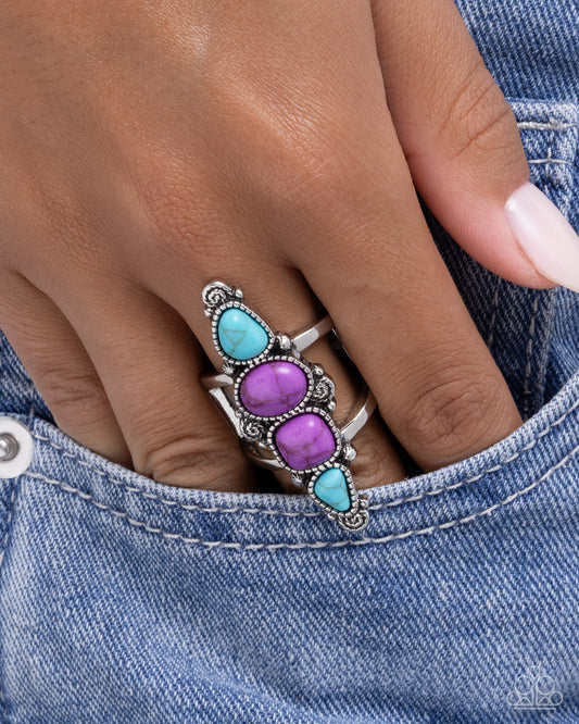 Silver ring with purple and turquoise stones on a hand wearing denim jeans.