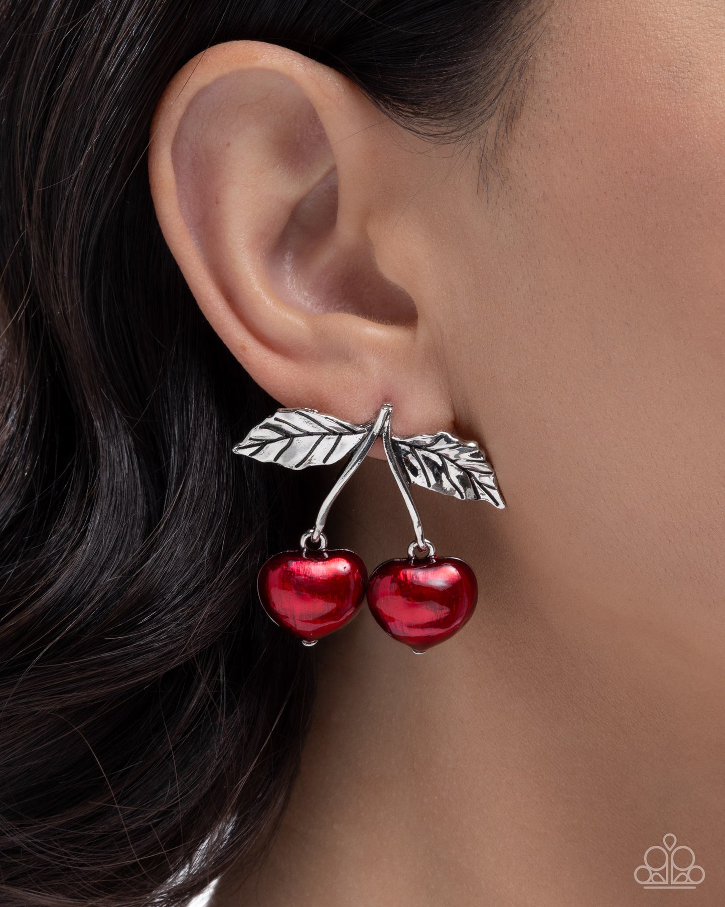 Red cherry earrings with silver leaves worn by a person