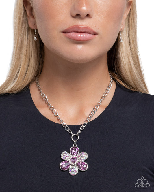 Woman wearing a silver chain necklace with a pink flower pendant on a black background