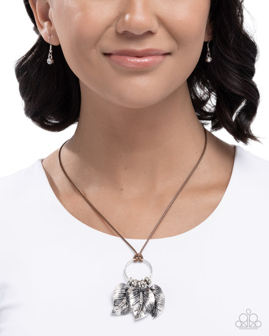 Woman wearing a silver necklace with leaf pendants on a white background