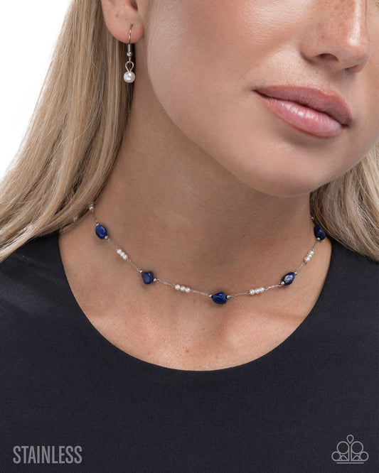 Close-up of a woman wearing a blue beaded necklace and earrings on a plain background.