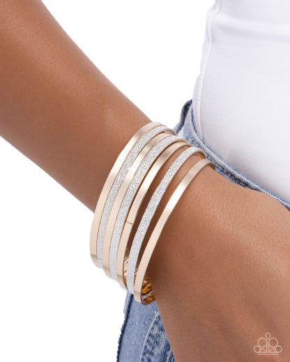 Stack of gold and silver bangles on a wrist with a white background