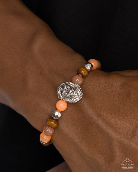 Bracelet with orange and brown beads and a silver lion head charm on a wrist against a dark background