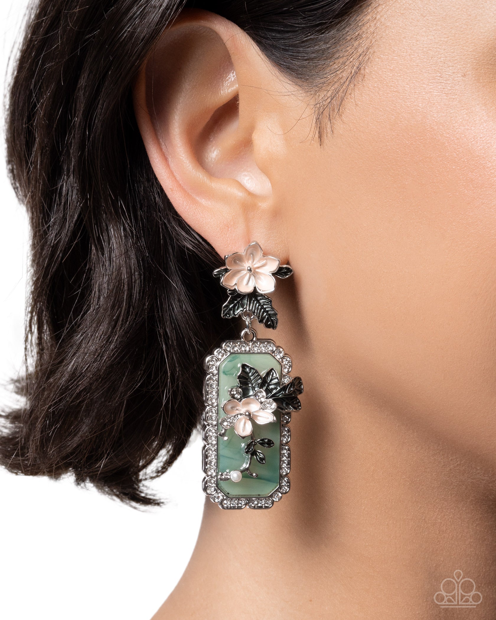 Close-up of an ear wearing a decorative earring with a green gemstone and butterfly design.