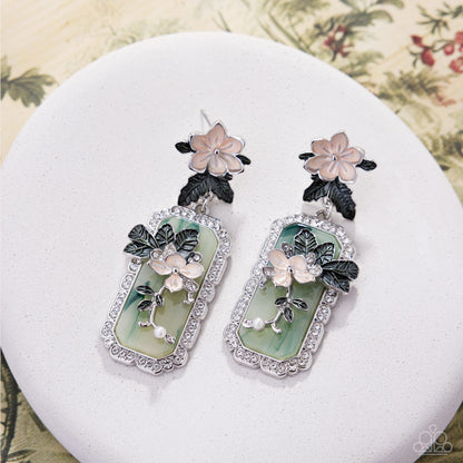 Pair of floral earrings on a white stand with a floral-patterned background