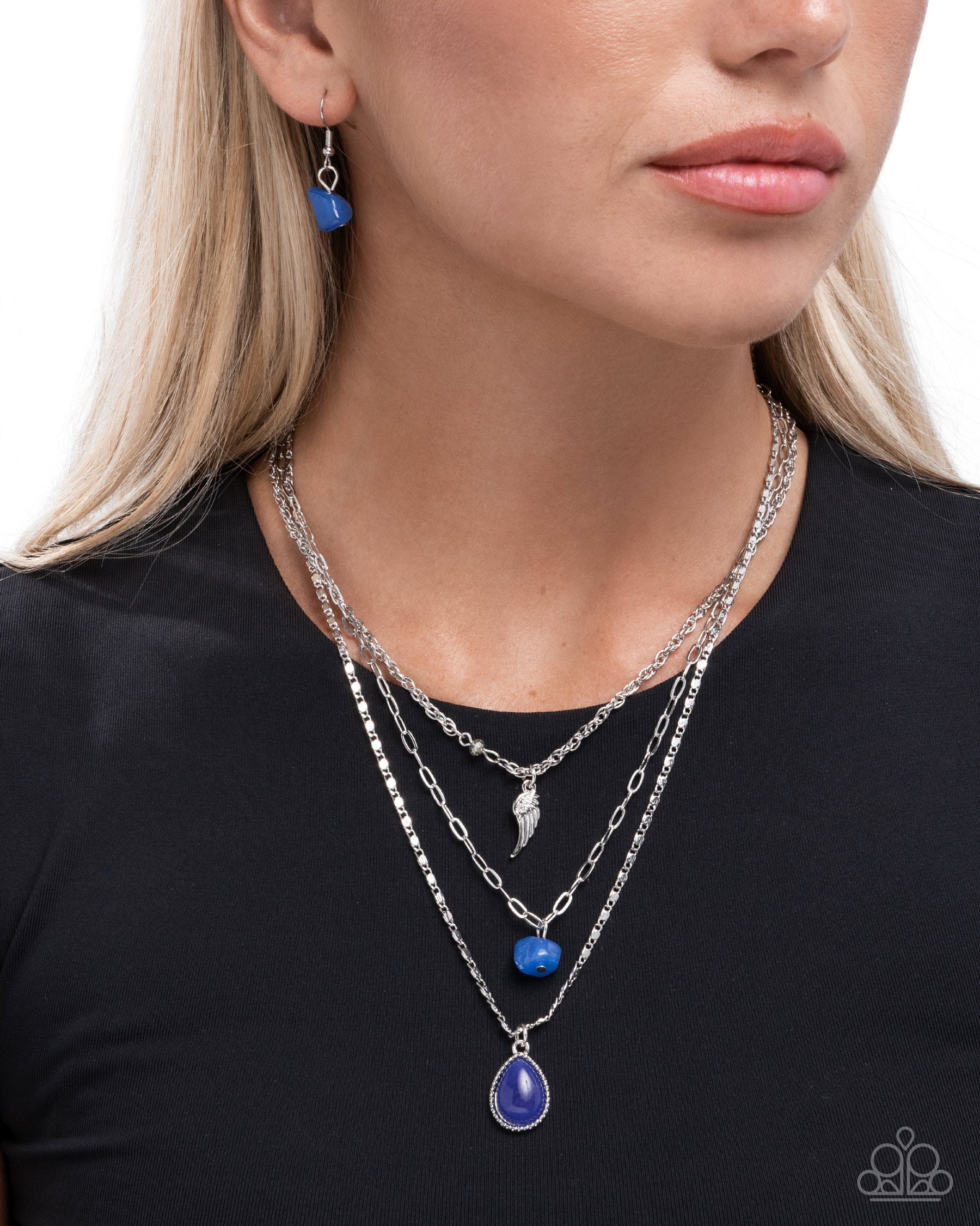 Woman wearing a layered necklace with blue pendant and matching earrings on a plain background