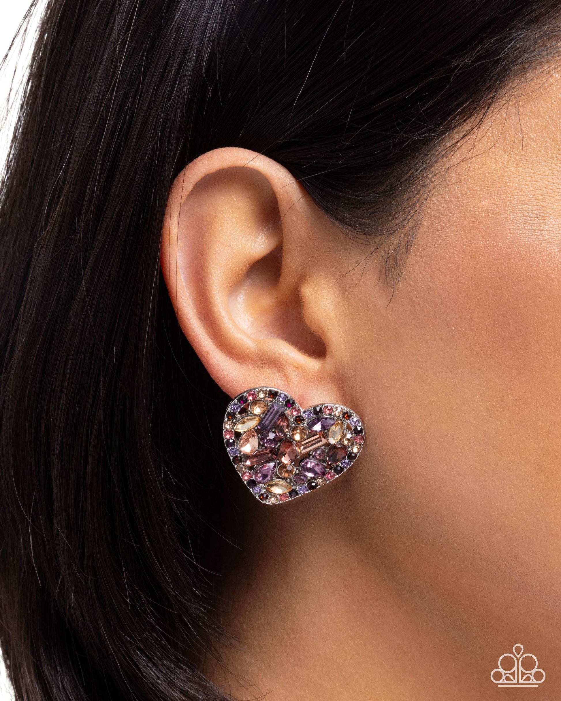 Heart-shaped earring with multicolored stones worn by a person with dark hair.