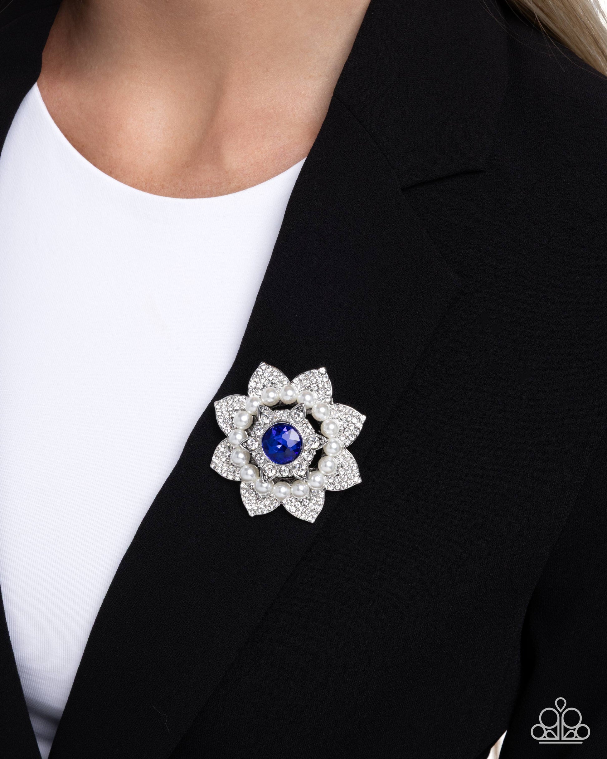 Close-up of a black blazer with a decorative brooch featuring a blue gemstone.