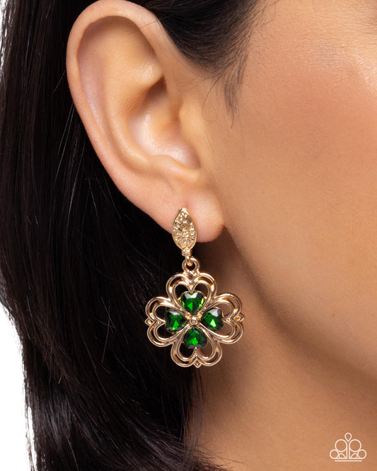 Gold earring with green gemstones worn by a person