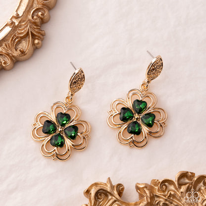 Gold earrings with green gemstones on a decorative background