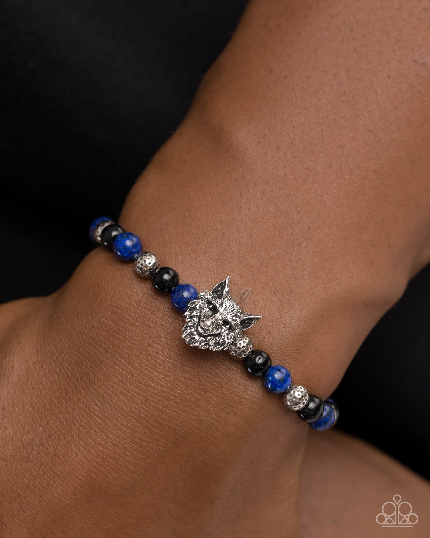Bracelet with blue and black beads and a silver wolf charm on a wrist.
