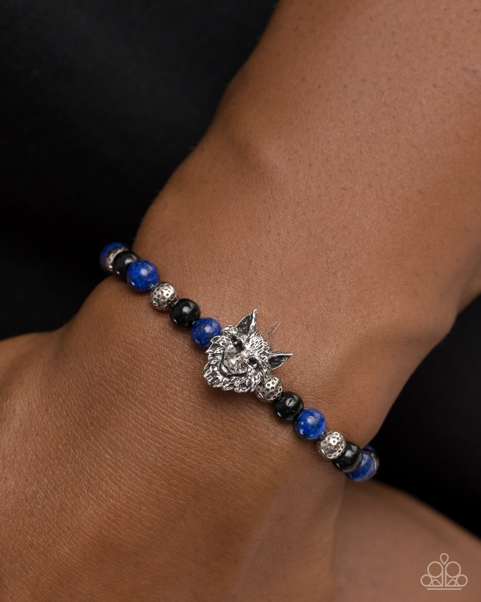 Bracelet with blue and black beads and a silver wolf charm on a wrist.