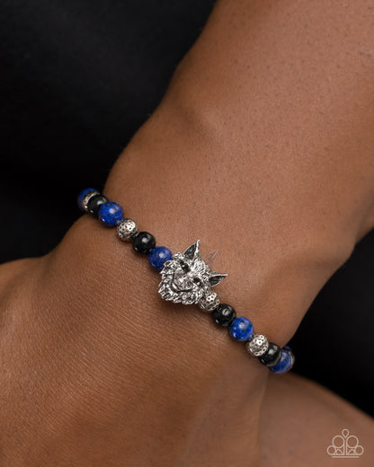 Bracelet with blue and black beads and a silver wolf charm on a wrist.