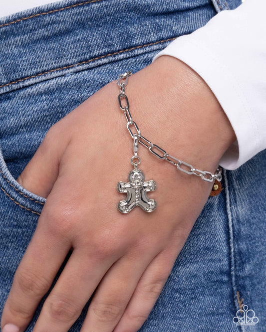 Silver chain bracelet with a gingerbread man charm on a wrist against a denim background