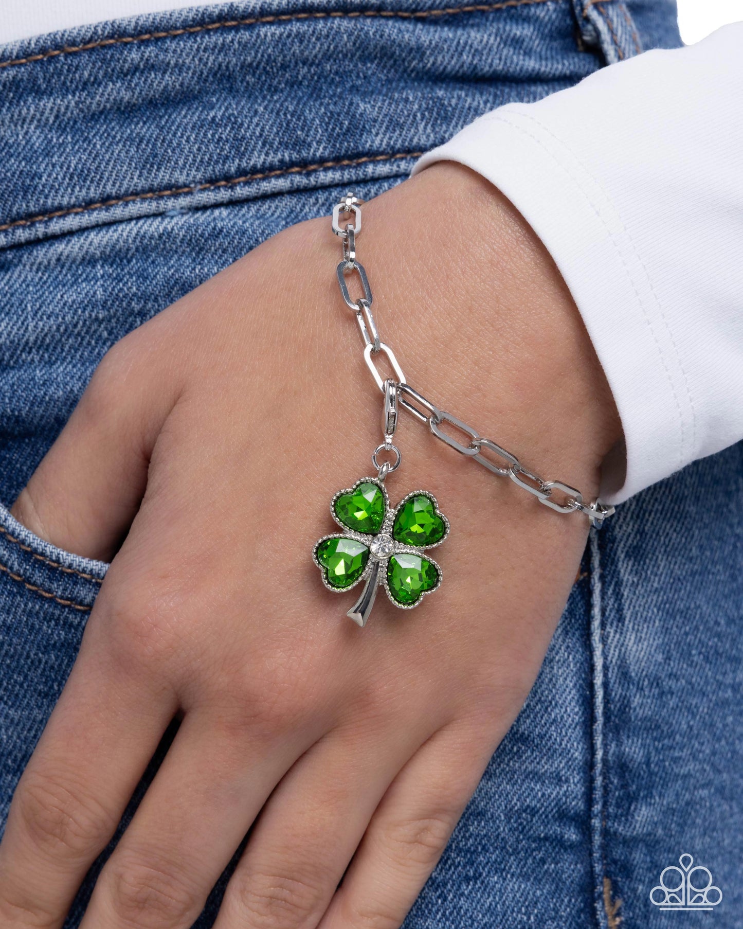 Silver bracelet with a green clover charm on a person's wrist against a denim background
