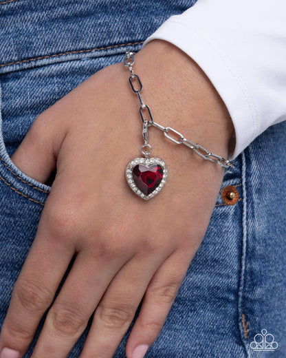 Bracelet with a heart-shaped red gemstone on a person's wrist against a denim background