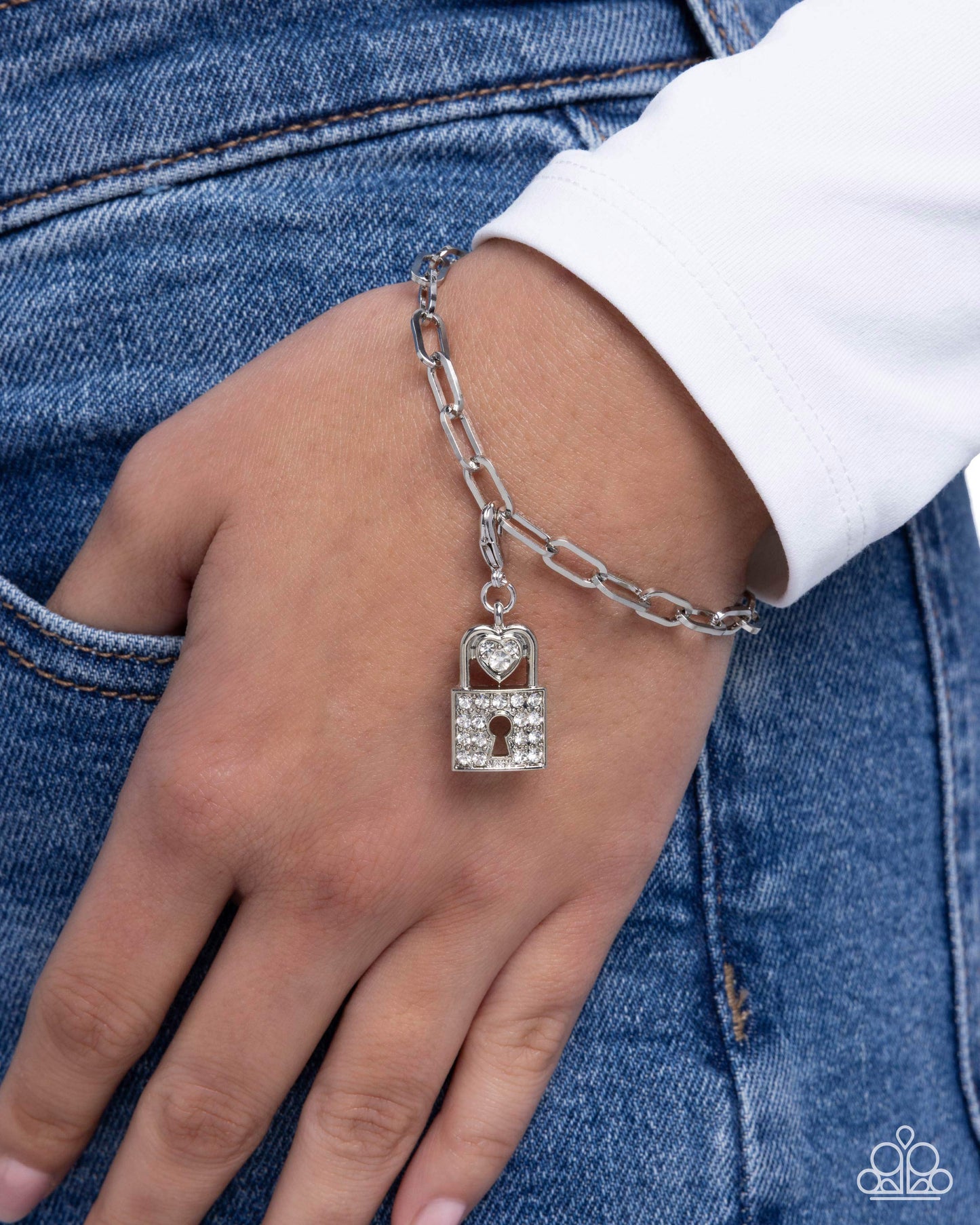 Silver chain bracelet with a lock charm on a wrist against a denim background