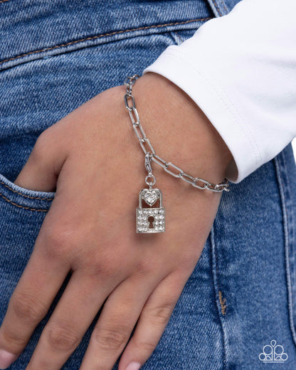 Silver chain bracelet with a lock charm on a wrist against a denim background