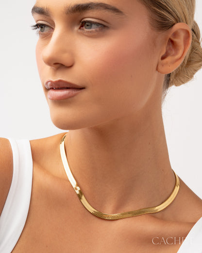 Woman wearing a gold necklace with a plain background