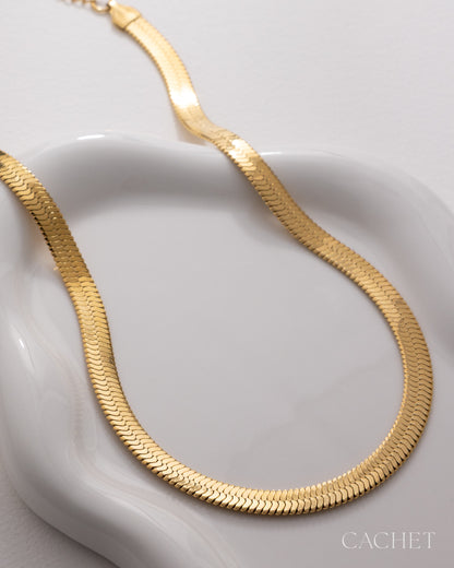 Gold necklace on a white dish with 'Cachet' branding.