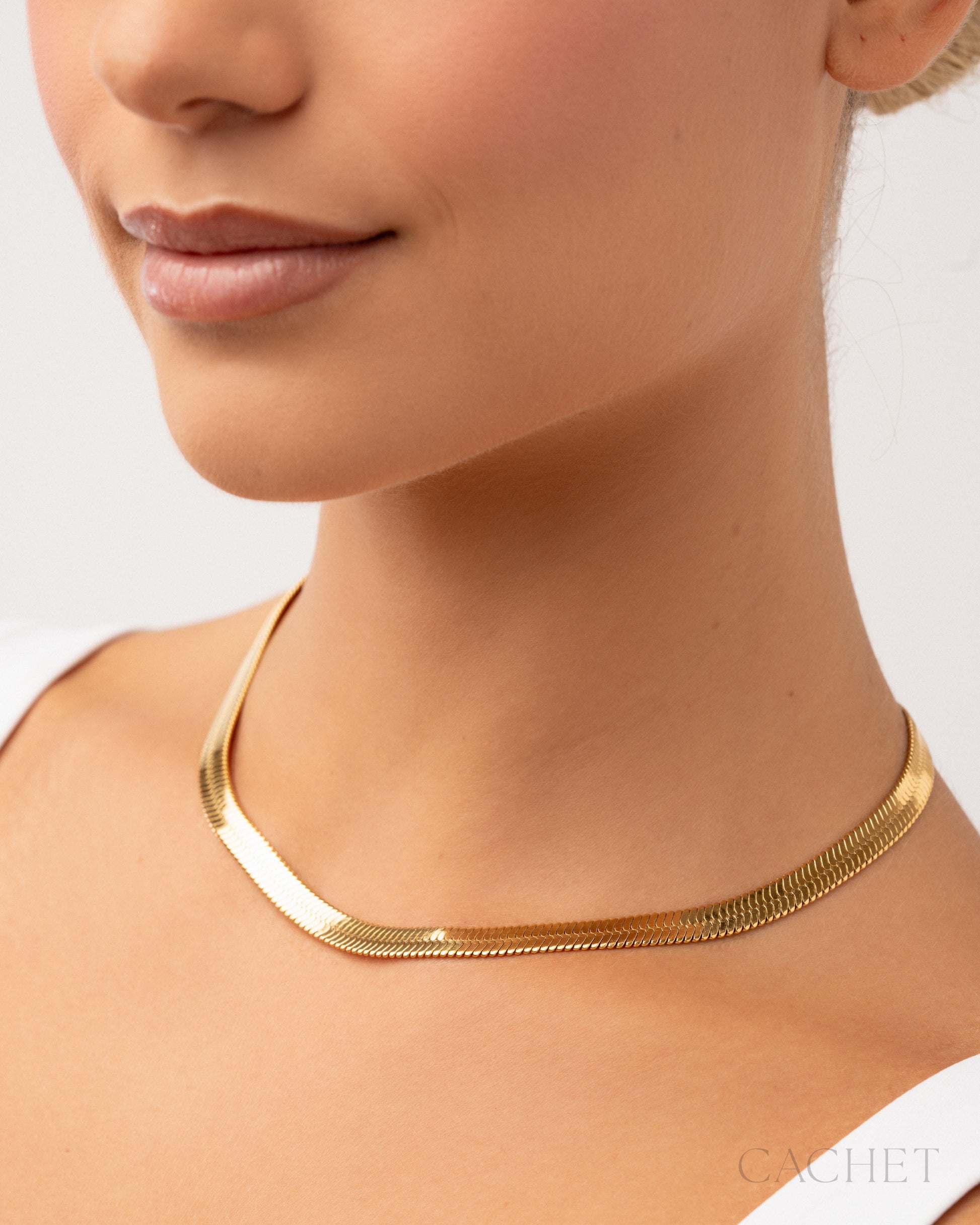 Gold necklace worn by a person on a plain background