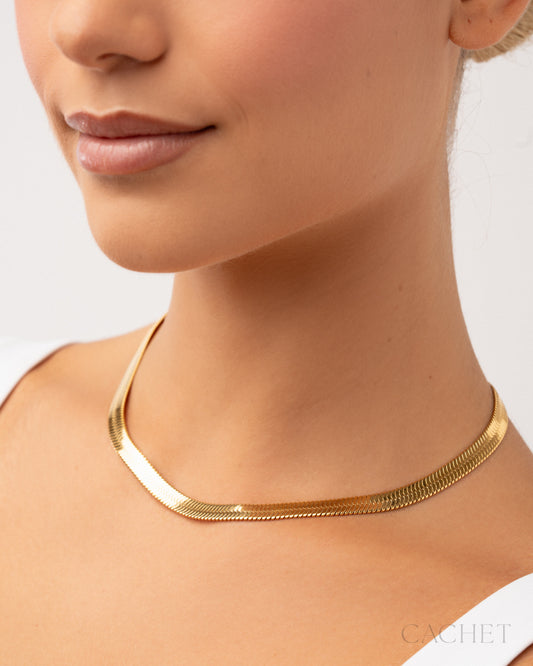 Gold necklace worn by a person on a plain background