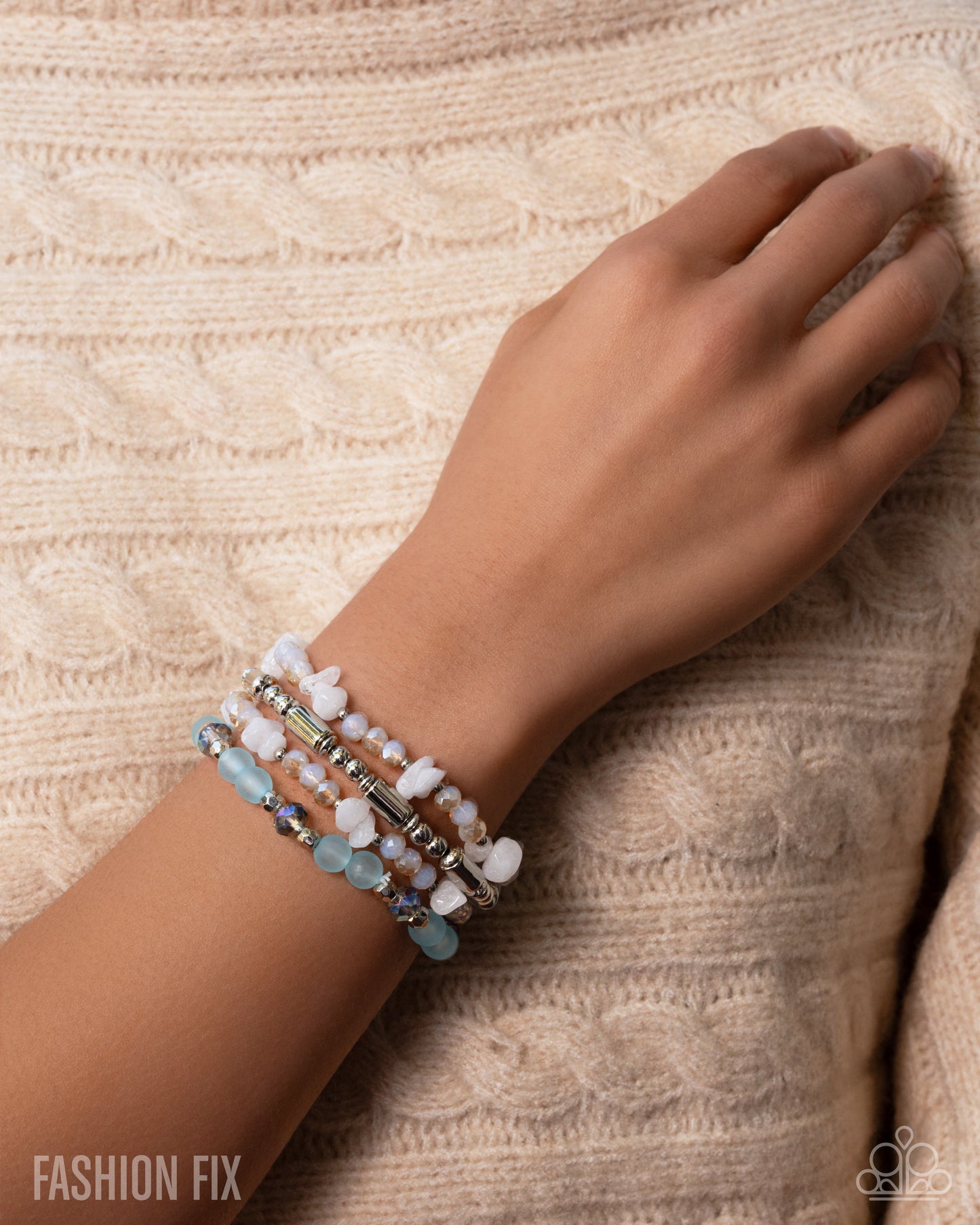 Hand wearing a bracelet with beads on a textured beige background