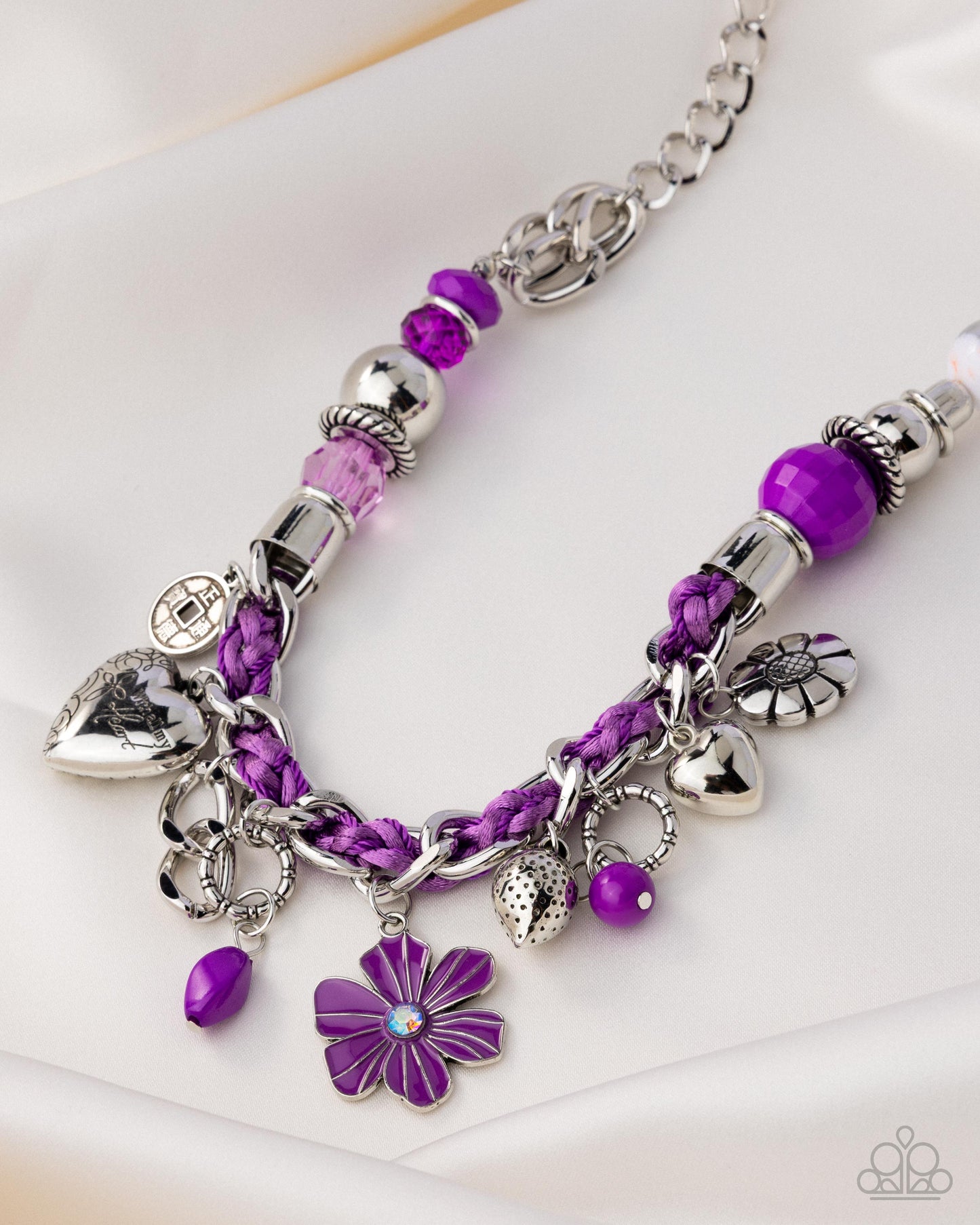 Purple beaded bracelet with silver charms on a white background