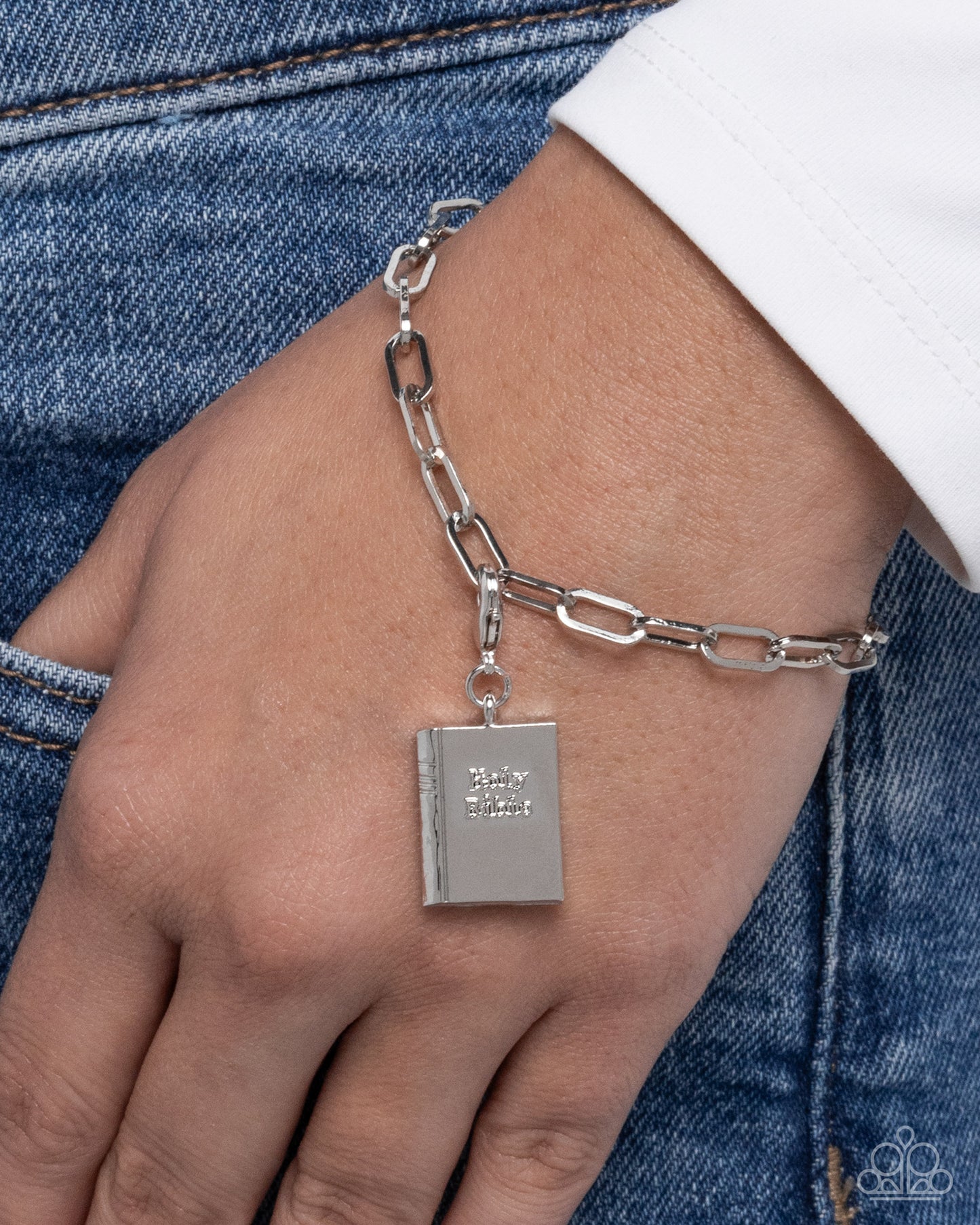Silver chain bracelet with a book-shaped charm on a wrist against a denim background