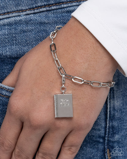 Silver chain bracelet with a book-shaped charm on a wrist against a denim background