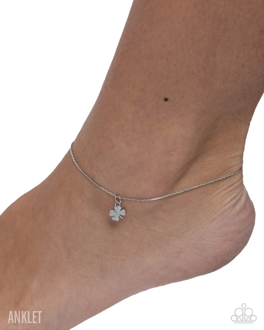 Silver anklet with a clover charm on a foot against a white background