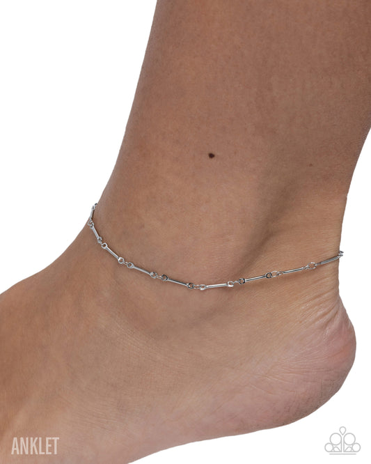A delicate silver anklet with a beaded chain design worn on a person's ankle, shown against a plain white background.