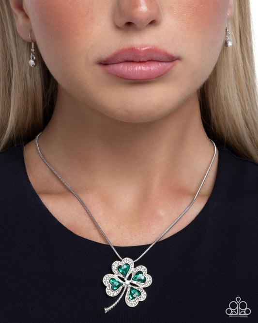 Close-up of a woman wearing a silver necklace with a green four-leaf clover pendant.