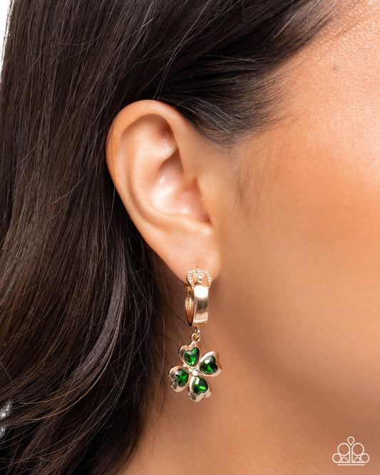 Gold earring with green clover charms worn by a person