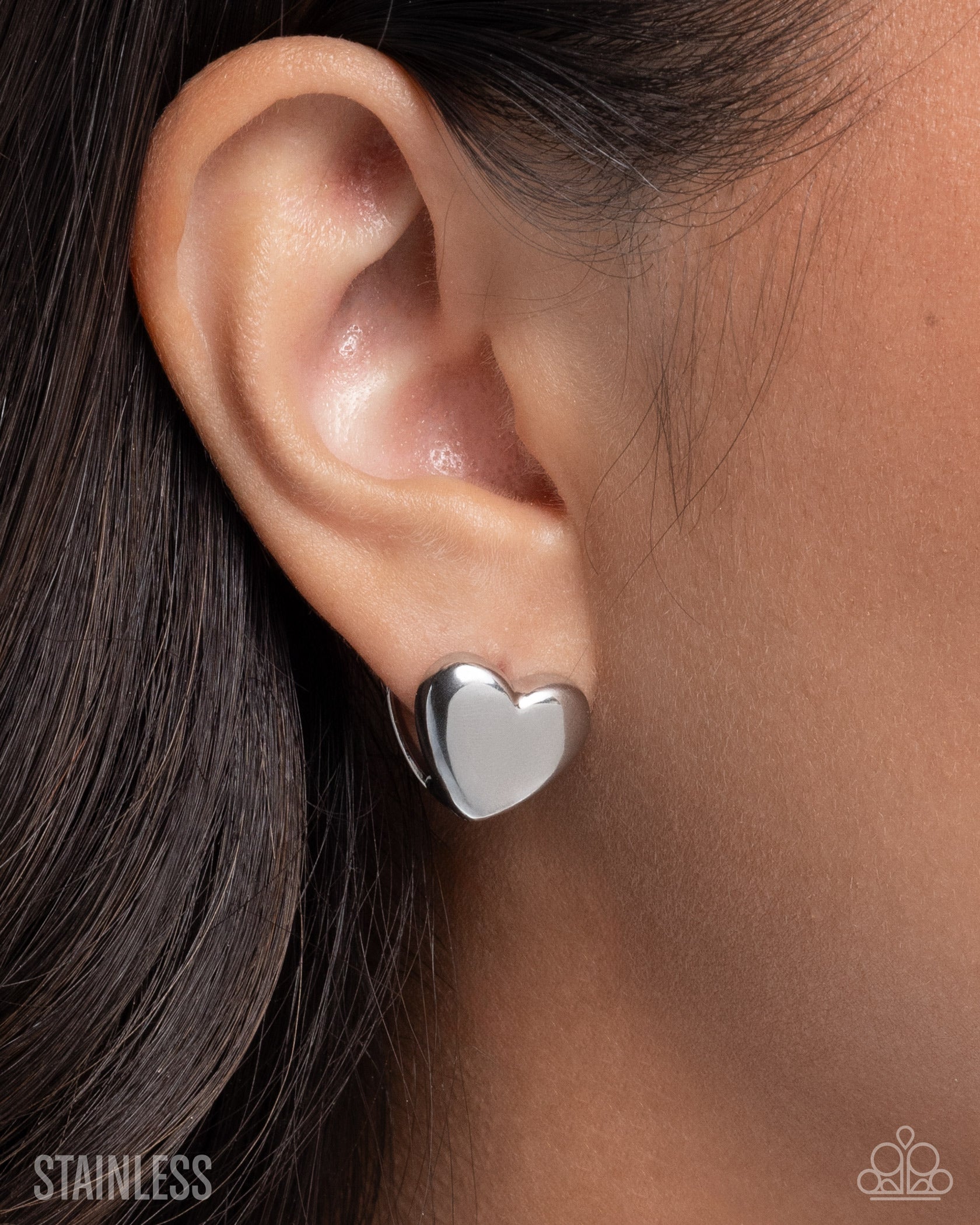 Silver heart-shaped earring worn on an ear with a blurred background