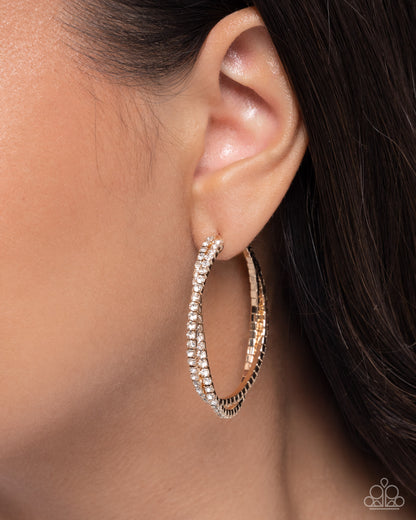 Close-up of an ear wearing a gold hoop earring with clear stones.