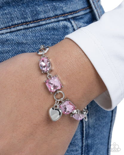 Pink beaded bracelet with heart charm on wrist against denim background
