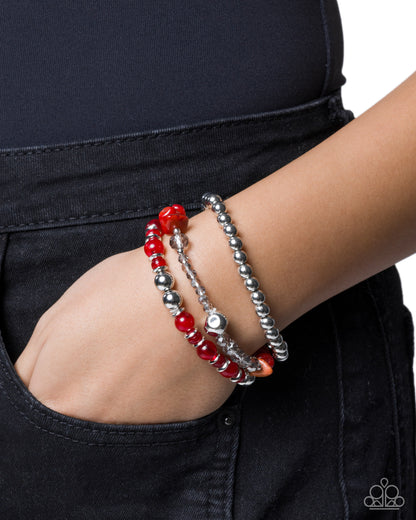 Person wearing a red beaded bracelet on a plain background