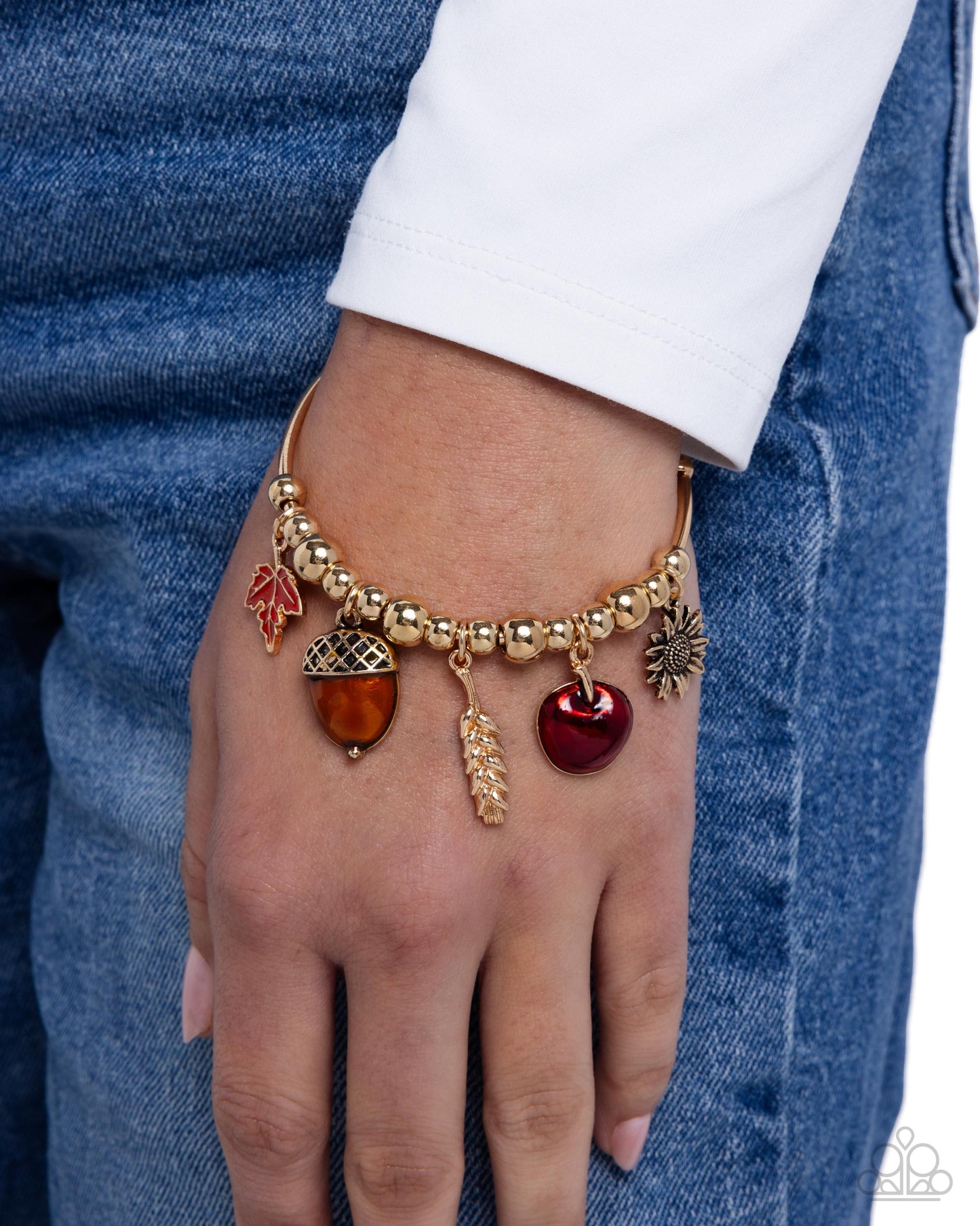 Gold bracelet with charms on a wrist against a denim background