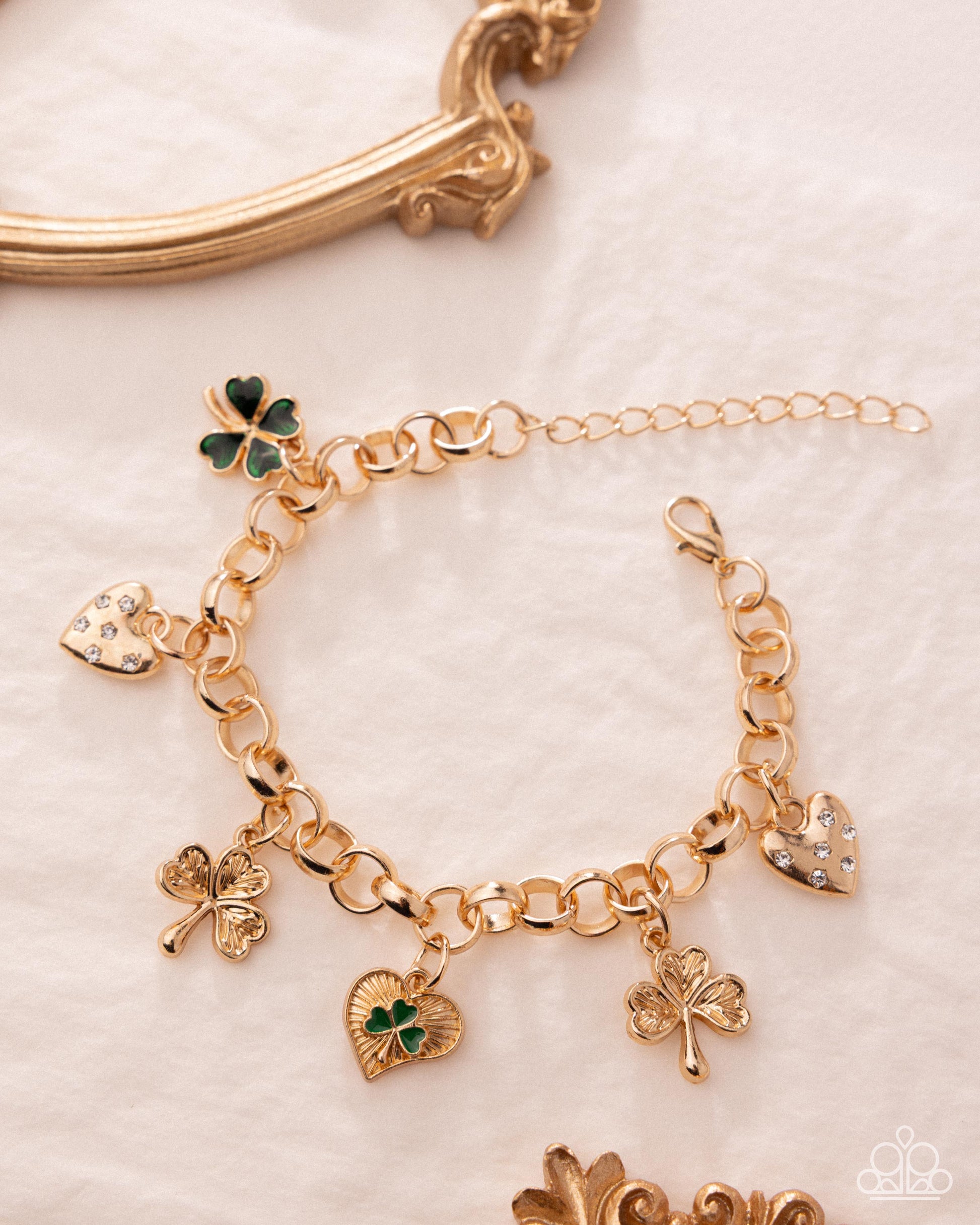 Gold bracelet with shamrock and heart charms on a light background