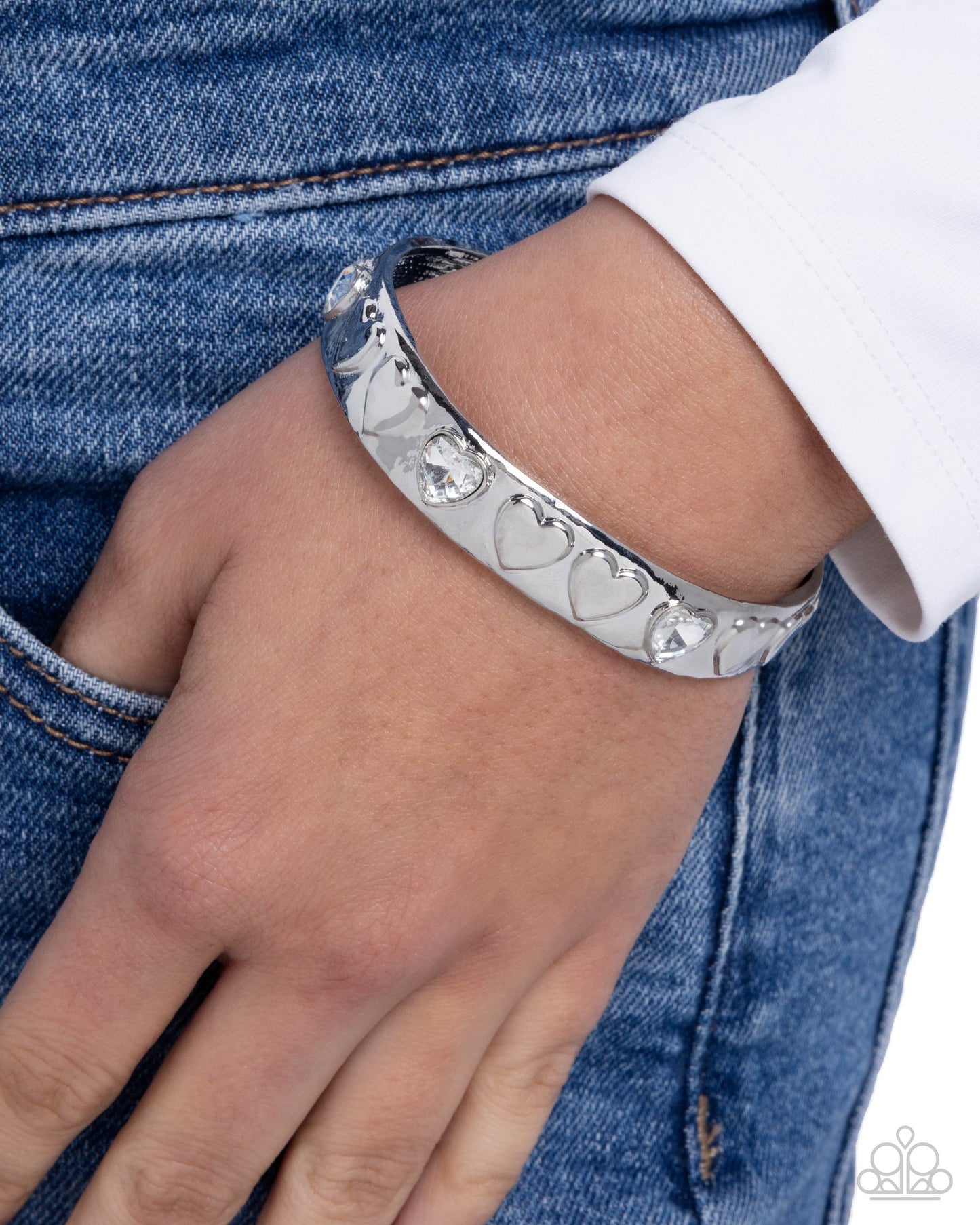 Silver bracelet with heart designs on a wrist against a denim background