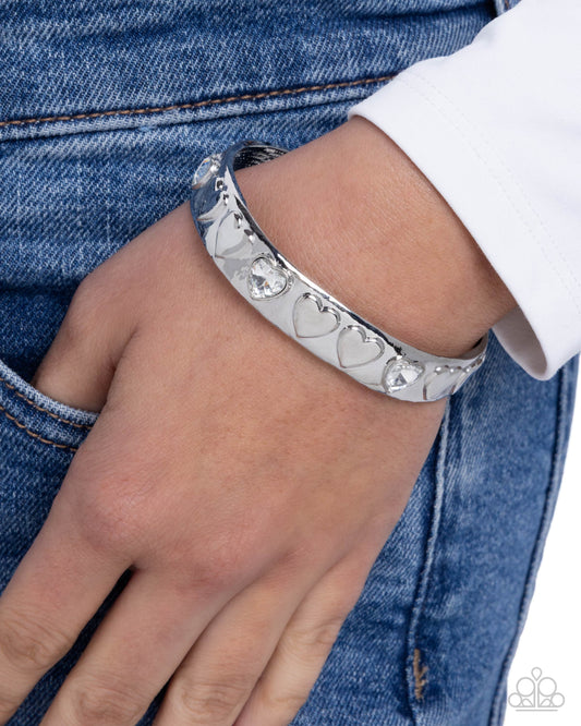 Silver bracelet with heart designs on a wrist against a denim background