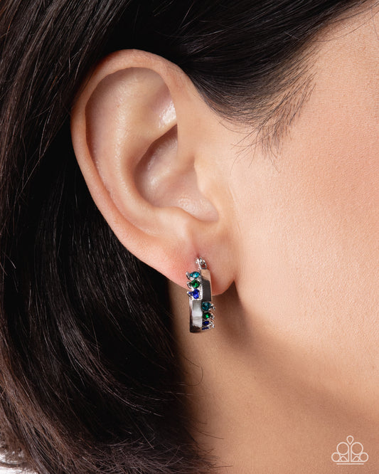 Close-up of an ear wearing a silver earring with green and blue gemstones.